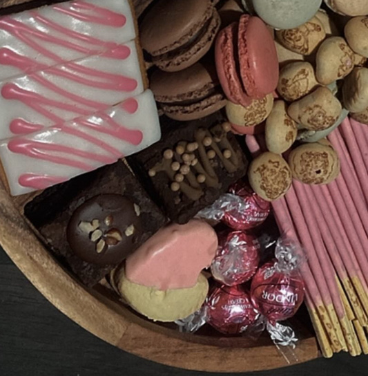A dessert platter featuring a variety of sweet treats including macarons, brownies, chocolate truffles, iced pastries, and Pocky sticks, high in sugar and fats.