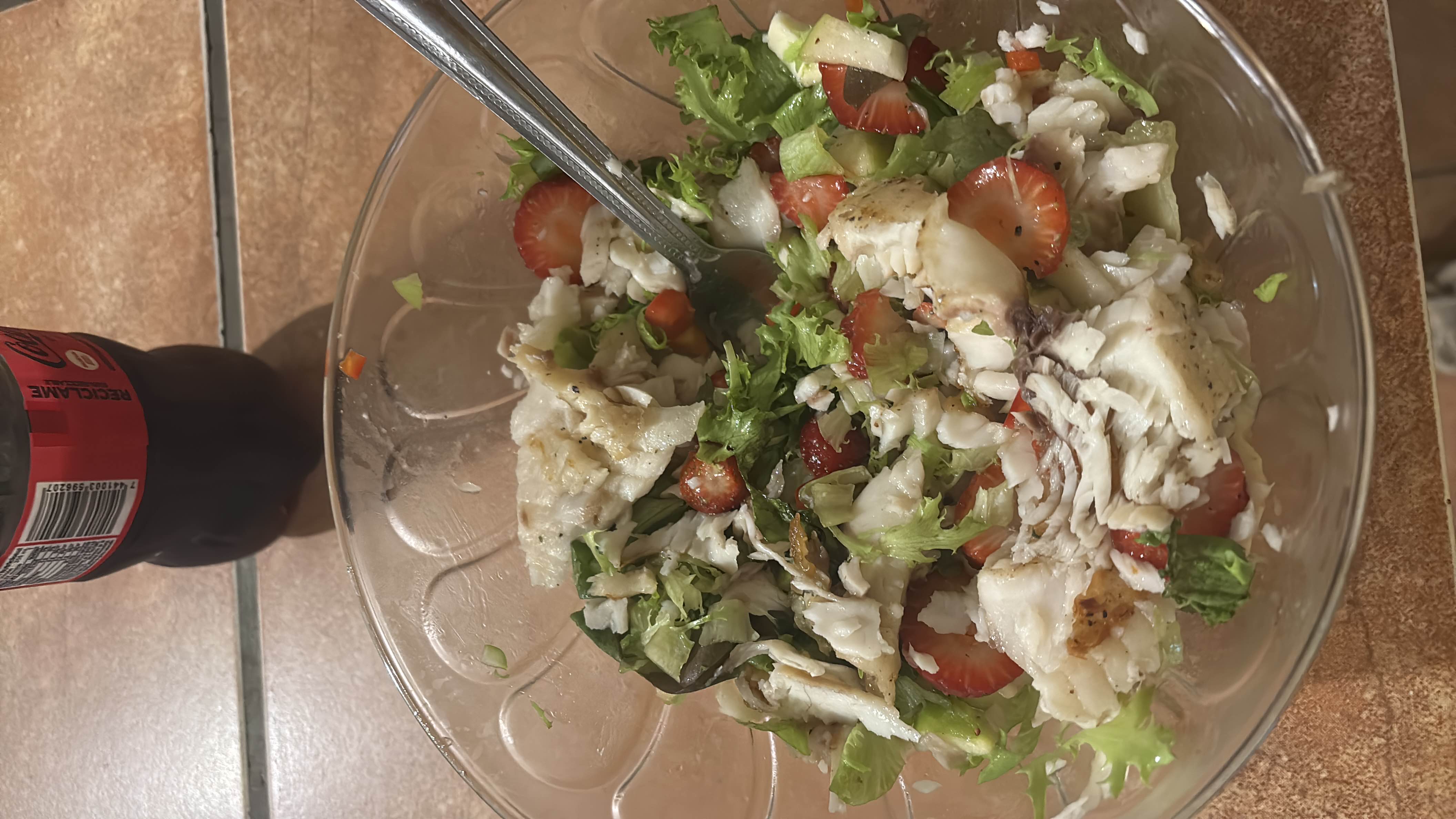 A healthy salad with grilled fish, fresh lettuce, strawberries, cucumber, and a drizzle of olive oil.