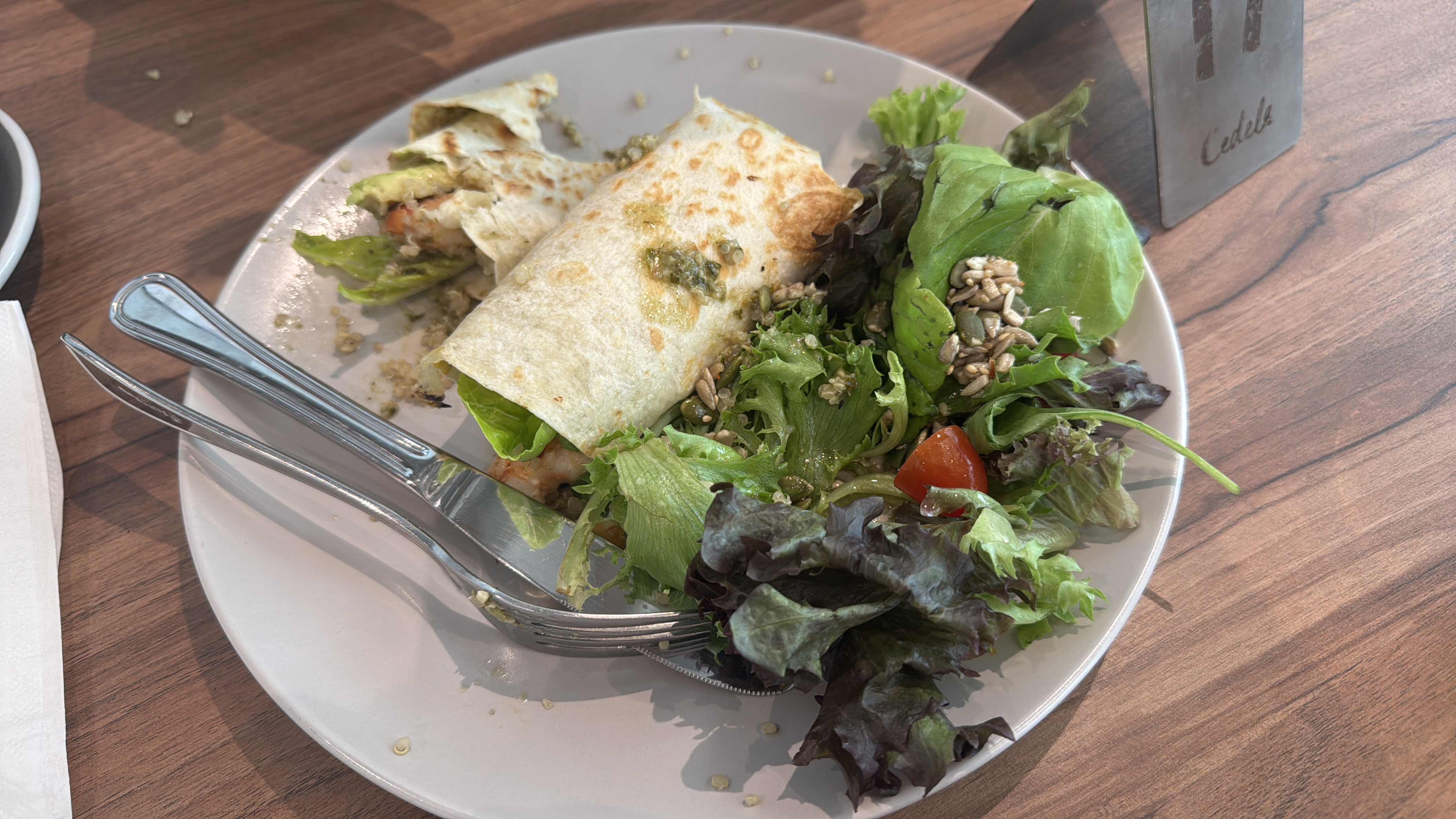 A healthy meal consisting of a grilled chicken wrap with avocado and a fresh green salad topped with sunflower seeds and dressing.
