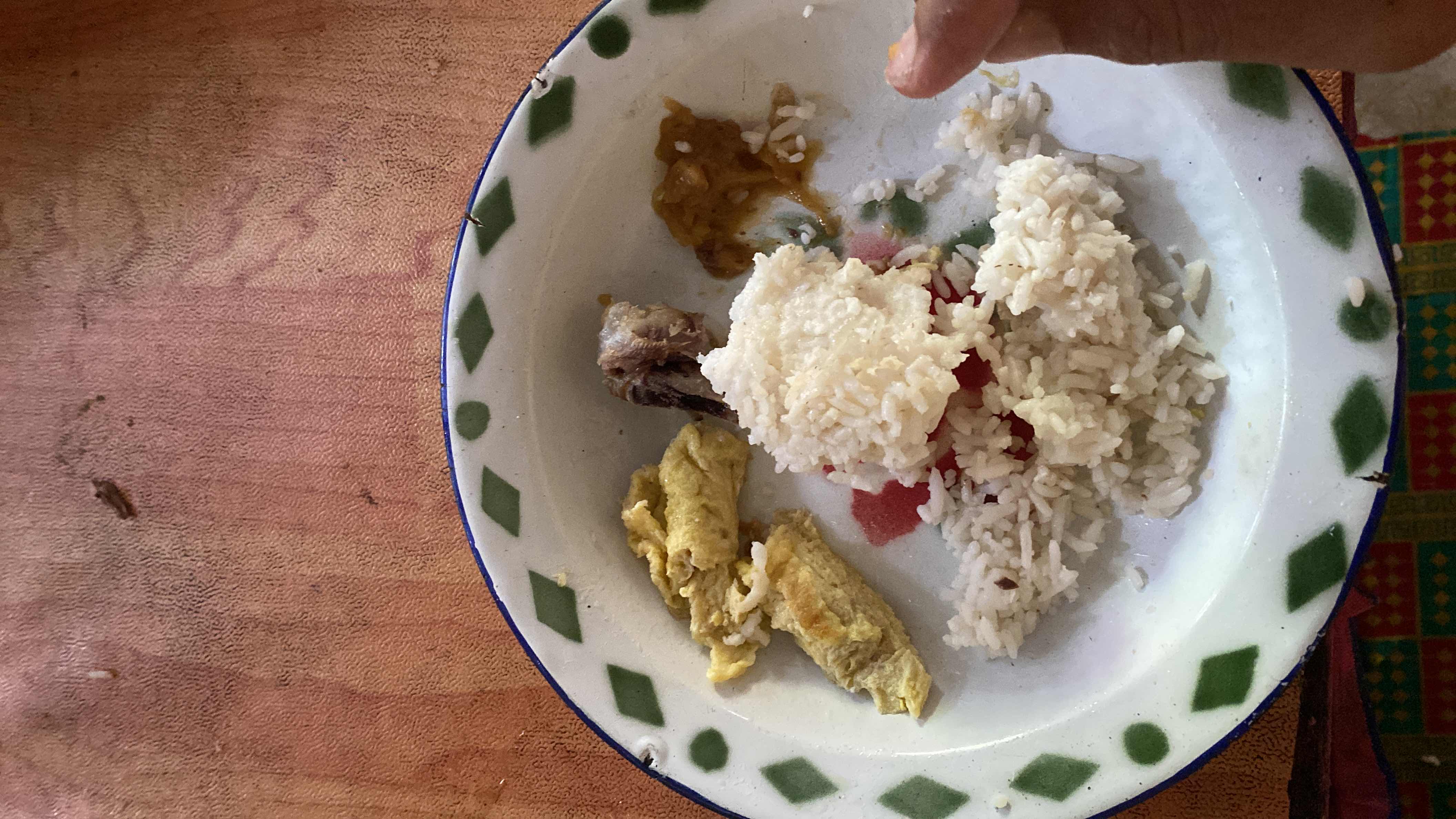 A plate containing white rice, scrambled egg, a small piece of meat, and some sauce, providing a balanced mix of carbohydrates, protein, and fats.