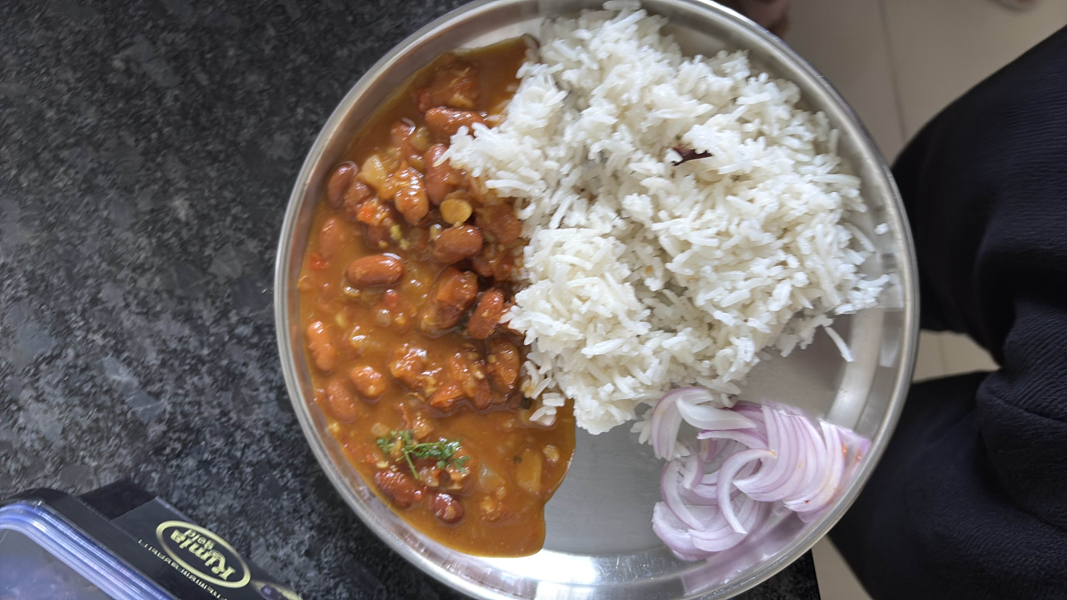 A nutritious meal consisting of rice, kidney bean curry, and sliced onions, providing a balanced mix of carbohydrates, protein, and essential nutrients.