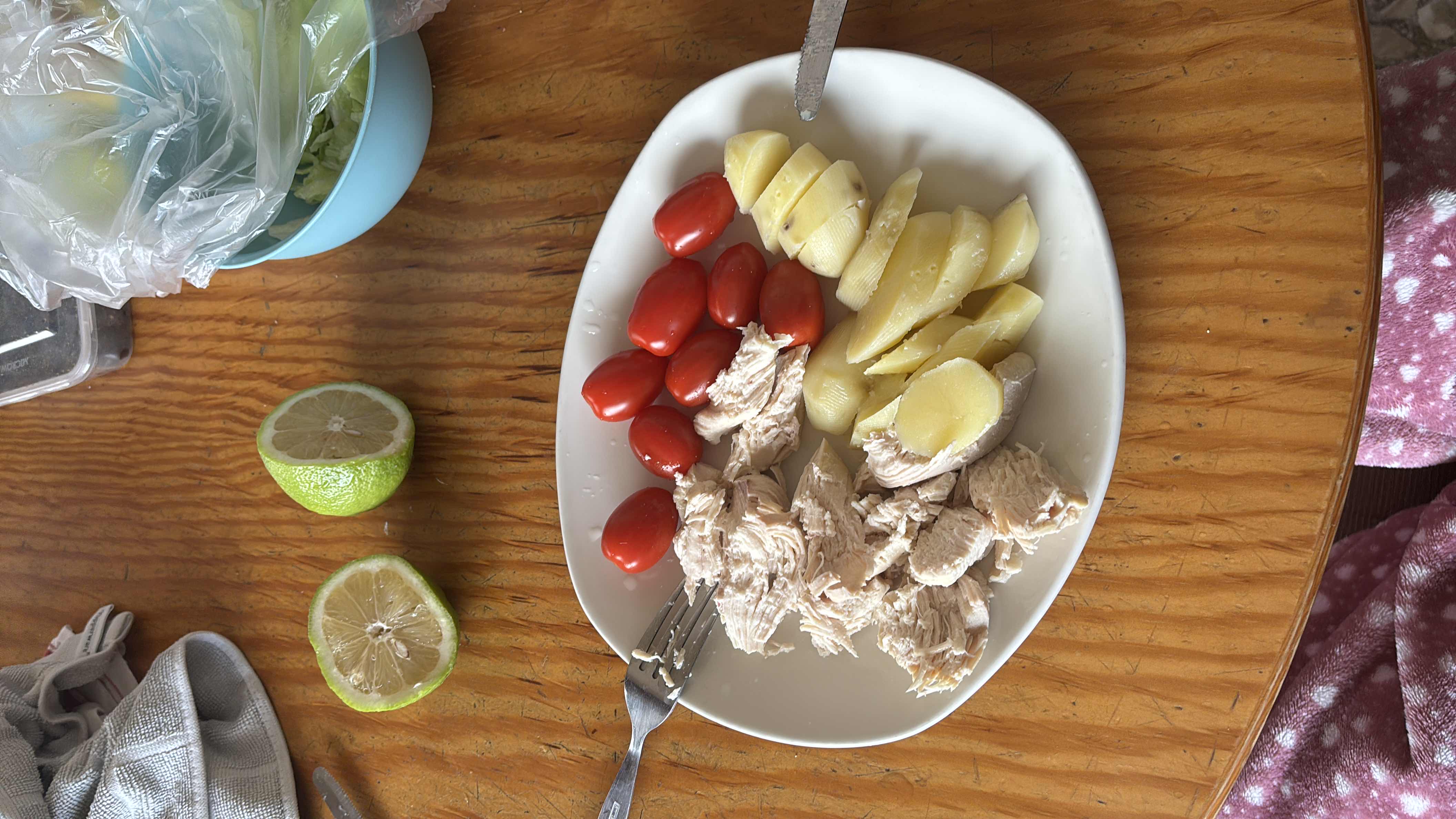 A healthy meal consisting of boiled chicken breast, boiled potatoes, cherry tomatoes, and lime, providing a balanced mix of protein and carbohydrates with minimal fats.