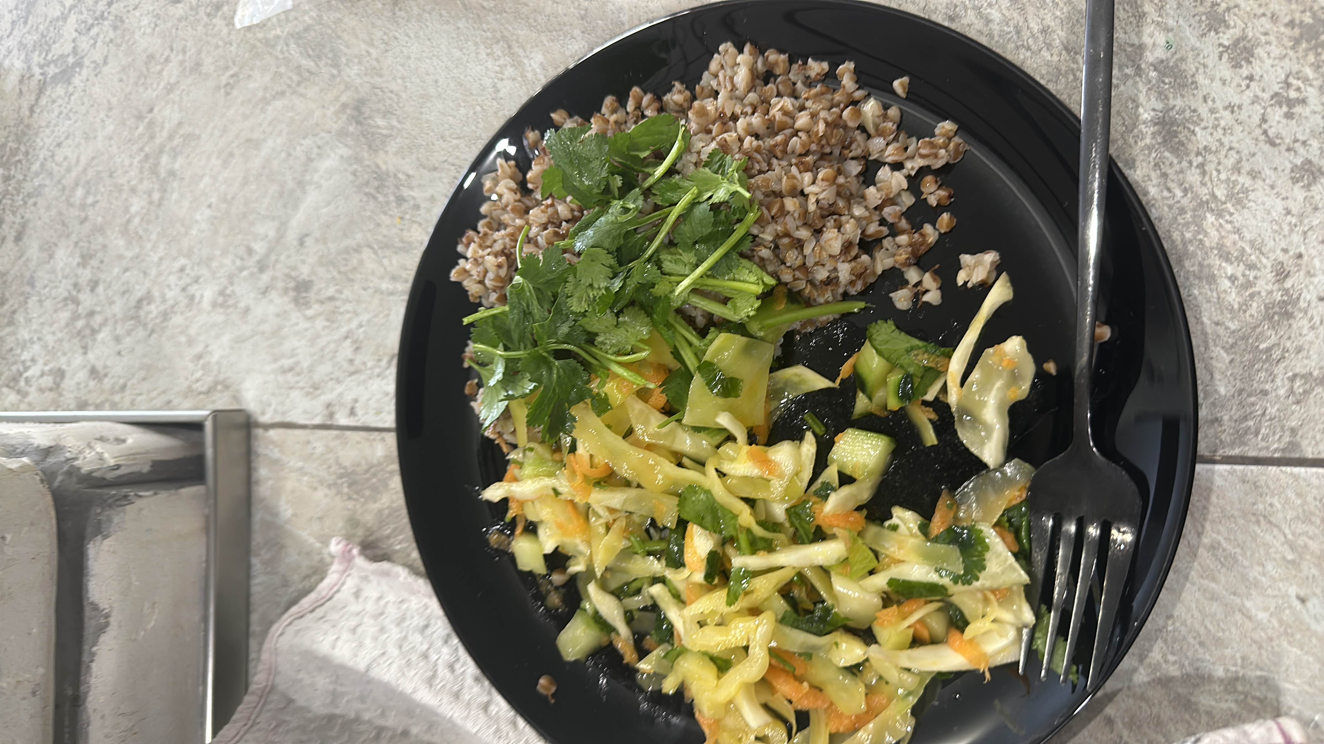 A healthy meal consisting of buckwheat, fresh vegetable salad with cabbage, carrot, cucumber, cilantro, and seaweed, dressed with a light oil-based dressing.