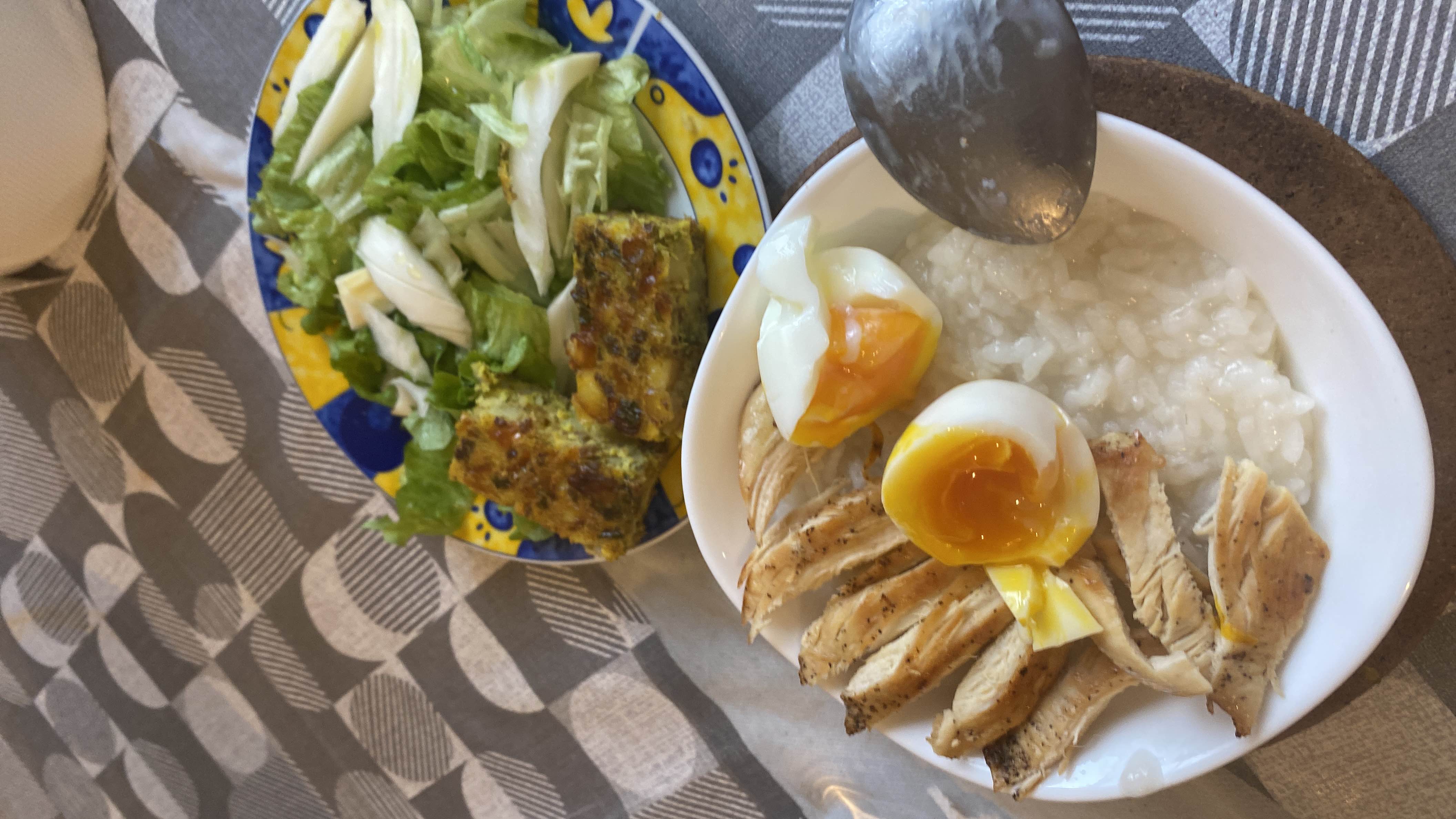 A balanced meal consisting of grilled chicken breast, soft-boiled eggs, rice porridge, a fresh lettuce salad, and a vegetable omelette.