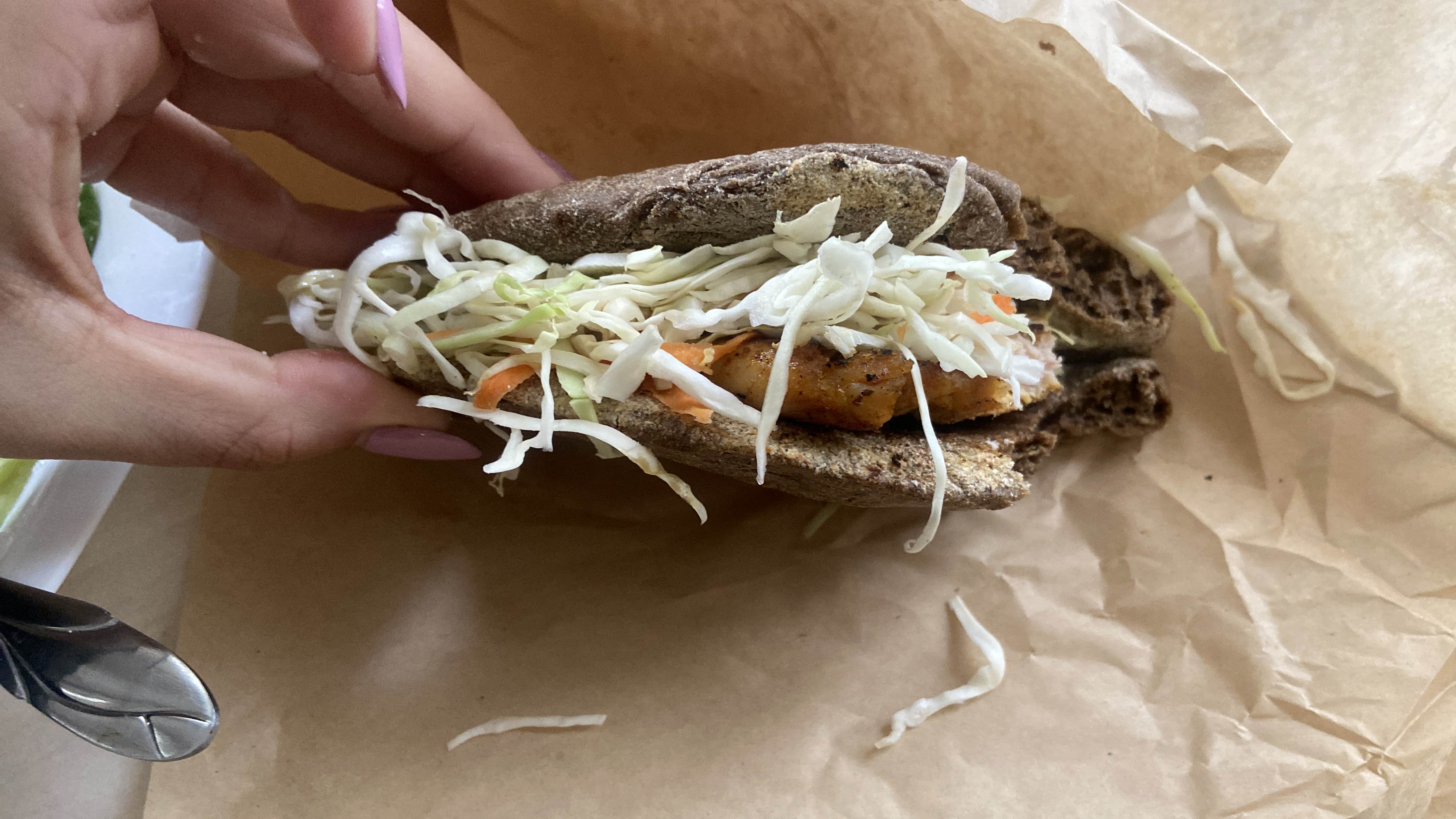A healthy whole wheat pita sandwich filled with grilled chicken, shredded cabbage, carrots, and a light sauce.