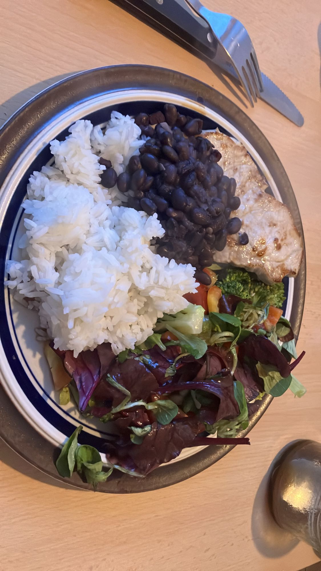 Prato com arroz, bife de porco, molho de salada, salada e feijão de colts